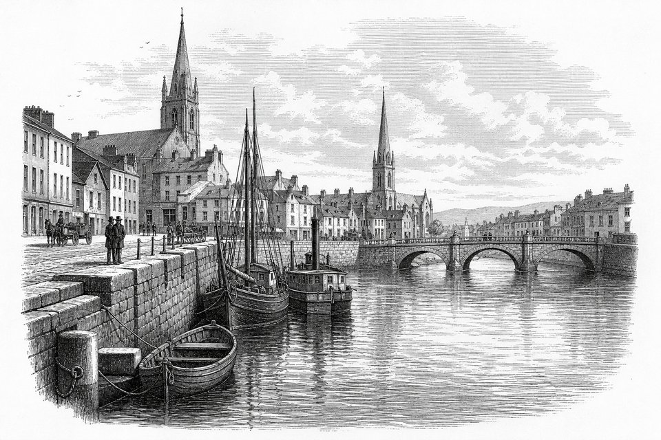 A river quay in an Irish city with a stone embankment, moored boats and church spires behind